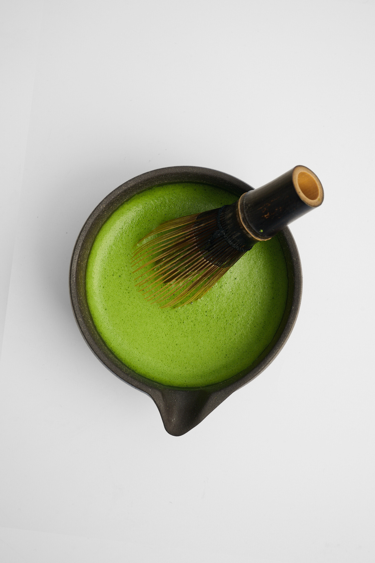 Green tea mixture in a black bowl with a whisk on a white background